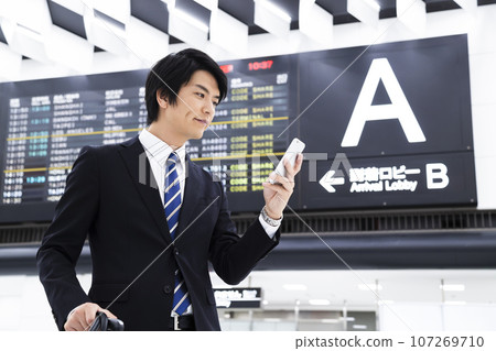 Young businessman on a business trip from the airport while looking at his smartphone 107269710