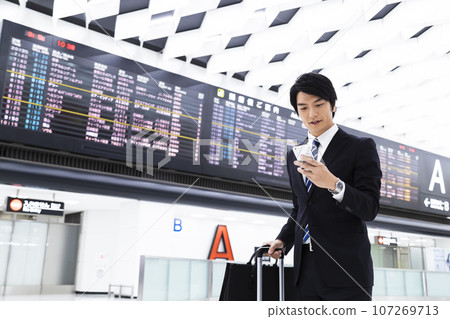 年輕商人從機場出差,同時看著他的智慧型手機 年輕商人從機場出差,同時看著他的智慧型手機 107269713