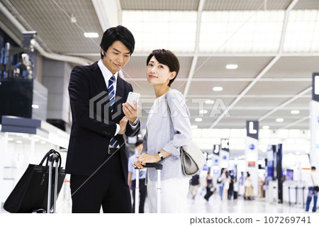 Young male and female businessmen on a business trip from the airport while looking at their smartphones Young male and female businessmen on a business trip from the airport while looking at their smartphones 107269741