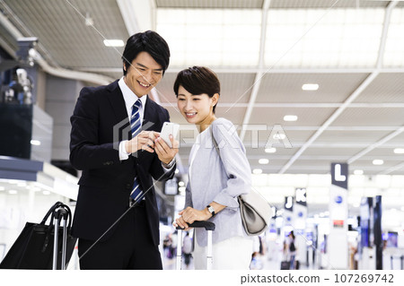 從機場出差的年輕男女商人一邊看智慧型手機 107269742