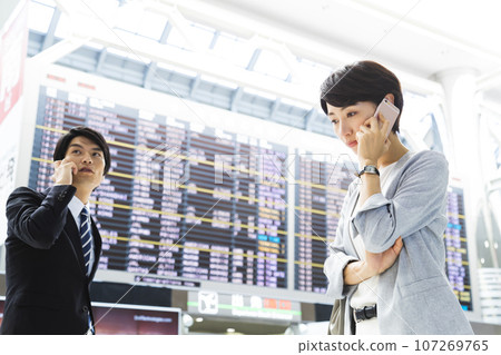 Young male and female businessmen on a business trip from the airport while looking at their smartphones 107269765