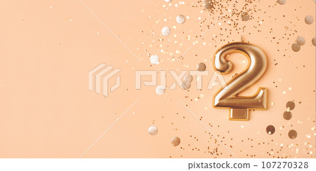Gold candle in the form of number two peach background with confetti. 107270328