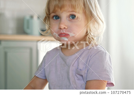 Baby girl enjoying ice cream. Pretty little toddler eating an ice-cream indoors, at home. Dining room background. Small child eats plombir and cream messy on her mouth. Cute kid with tasty sweet food. Baby girl enjoying ice cream. Pretty little toddler eating an ice-cream indoors, at home. Dining room background. Small child eats plombir and cream messy on her mouth. Cute kid with tasty sweet food. 107270475