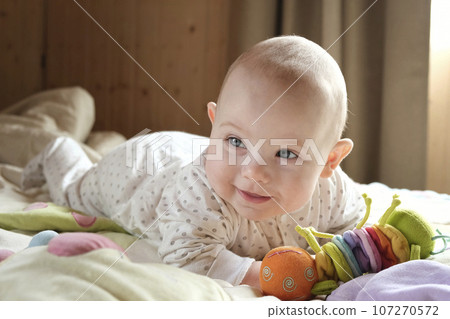 Smiling baby girl learning to crawl and playing with colorful toys in white sunny bedroom. Smiling baby girl learning to crawl and playing with colorful toys in white sunny bedroom. 107270572