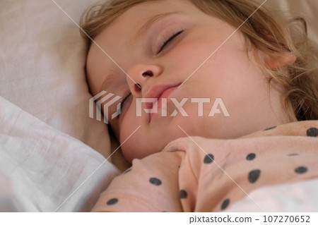 Peaceful adorable baby sleeping on a bed at home. Slumbering little child. Two year old girl sleeps peaceful at domestic room interior background. Serene dream. Cute face close up. Deep kid slumber Peaceful adorable baby sleeping on a bed at home. Slumbering little child. Two year old girl sleeps peaceful at domestic room interior background. Serene dream. Cute face close up. Deep kid slumber 107270652
