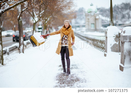 smiling stylish female in brown hat and scarf in camel coat 107271375