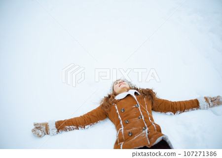 happy stylish woman in brown hat and scarf laying on snow 107271386