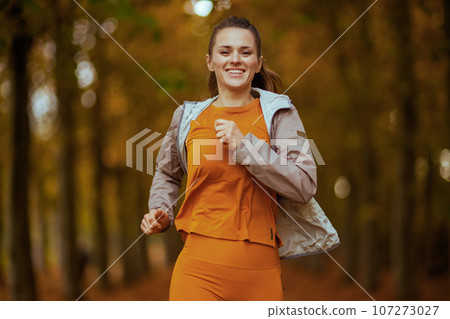 smiling trendy woman in fitness clothes in park running 107273027
