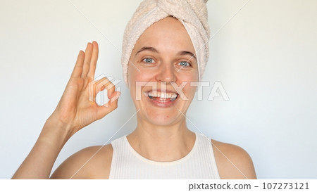 Happy joyful beautiful young woman with bath towel on head isolated over white background showing ok gesture approved sign likes her morning routine looking smiling at camera. Happy joyful beautiful young woman with bath towel on head isolated over white background showing ok gesture approved sign likes her morning routine looking smiling at camera. 107273121