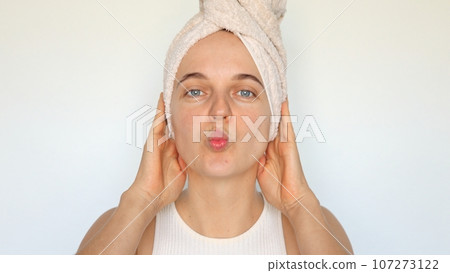 Flirting cheerful beautiful young woman with bath towel on head isolated over white background sending air kissing looking at camera with rounded lips. 107273122