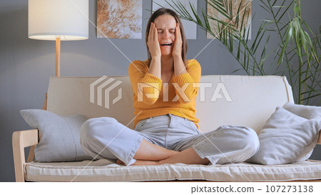 Upset depressed young woman feeling depress sitting on couch, sad desperate ashamed female in trouble having problem, crying alone at home wearing casual clothing. 107273138