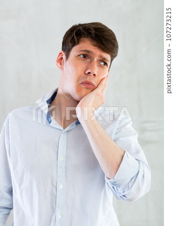 Unhappy man having a toothache in living room 107273215