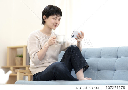 Young woman sitting on sofa and using smartphone Young woman sitting on sofa and using smartphone 107273378