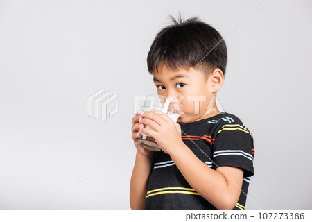 Little cute kid boy 5-6 years old smile drinking fresh water from glass in studio shot isolated on white background, Asian children preschool, Daily life health 107273386