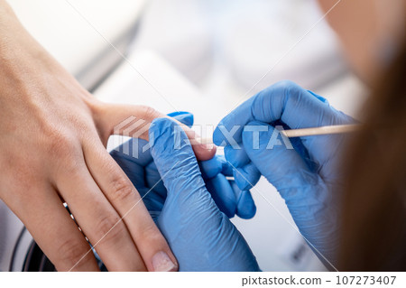 Nail care procedure in a beauty salon. Female hands and tools for manicure, process of performing manicure in beauty salon. Concept spa body care. Gloved hands of a skilled manicurist cutting cuticles Nail care procedure in a beauty salon. Female hands and tools for manicure, process of performing manicure in beauty salon. Concept spa body care. Gloved hands of a skilled manicurist cutting cuticles 107273407