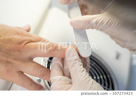 Nail care procedure in a beauty salon. Female hands and tools for manicure, process of performing manicure in beauty salon. Gloved hands of a skilled manicurist cutting cuticles. Concept spa body care 107273423