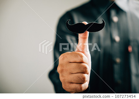 A man's thumb holds a mustache, signifying support for those affected by Prostate Cancer a powerful image for men's healthcare and World Cancer Day. A man's thumb holds a mustache, signifying support for those affected by Prostate Cancer a powerful image for men's healthcare and World Cancer Day. 107273454
