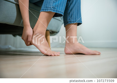 Asian beautiful female problems with foot at home, painful ankle injury, Young woman sitting on sofa holding her feet and stretch muscles have symptoms feeling pain, Health care and medical concept Asian beautiful female problems with foot at home, painful ankle injury, Young woman sitting on sofa holding her feet and stretch muscles have symptoms feeling pain, Health care and medical concept 107273509