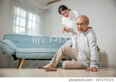 Dizziness elderly old man falling down lying on floor with walking stick and assistant nurse help to support, senior father fall on the ground and his daughter helping wake up and get up, accident 107273524