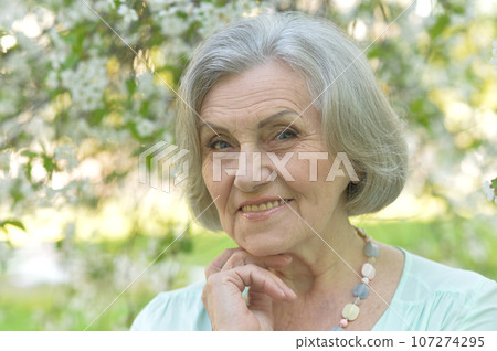 Close-up portrait of smiling elderly woman posing in summer park Close-up portrait of smiling elderly woman posing in summer park 107274295