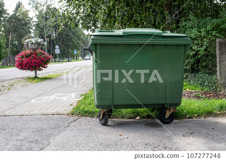 Green garbage container by the side of the street. Copy space 107277248