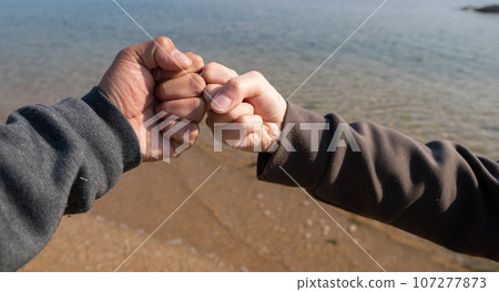 two people putting fists together two people putting fists together 107277873