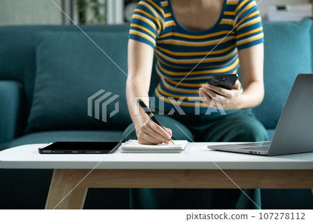 businessman use a smartphone and take notes in the notebook at the office desk in the morning. businessman use a smartphone and take notes in the notebook at the office desk in the morning. 107278112
