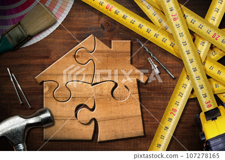 Wooden House made of Puzzle Pieces on Workbench with Work Tools 107278165