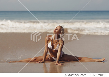 Stretching Leg-split on Seashore of Tanned Bikini Beach Woman 107279038