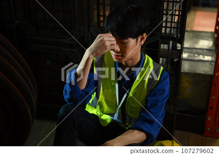 Depressed and tried male worker sitting alone in warehouse, having hard day on the work 107279602