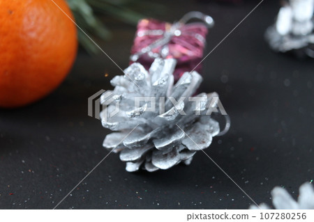 mandarin whole in the peel and a slice of fruit lie side by side on a black background next to a branch of spruce and a silver cone. New Year and Christmas. holiday attribute mandarin whole in the peel and a slice of fruit lie side by side on a black background next to a branch of spruce and a silver cone. New Year and Christmas. holiday attribute 107280256