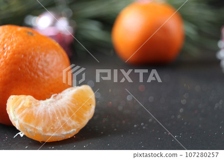 mandarin whole in the peel and a slice of fruit lie side by side on a black background next to a branch of spruce and a silver cone. New Year and Christmas. holiday attribute mandarin whole in the peel and a slice of fruit lie side by side on a black background next to a branch of spruce and a silver cone. New Year and Christmas. holiday attribute 107280257