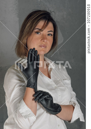 Portrait of confident lashmaker standing on gray background and putting on black medical glove, getting ready for work. 107280918