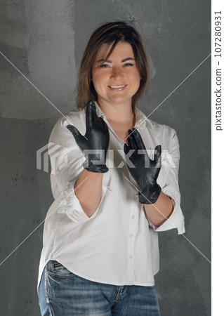 Wonderful lashmaker in black latex gloves standing against gray wall and stretching out arms, showing work consumable. Wonderful lashmaker in black latex gloves standing against gray wall and stretching out arms, showing work consumable. 107280931