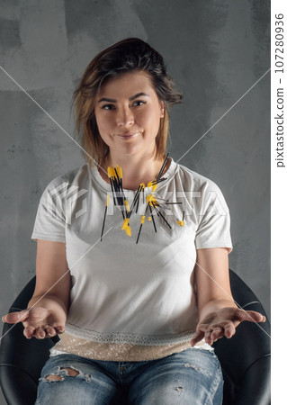Graceful young lashmaker sitting on chair on gray background, throwing up yellow eyelash extension brushes and smiling. Graceful young lashmaker sitting on chair on gray background, throwing up yellow eyelash extension brushes and smiling. 107280936