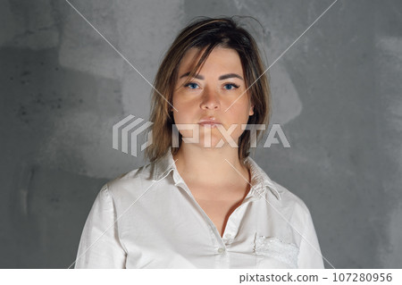 Portrait of gorgeous brunette with short hair standing against gray background and looking ahead without expression. Portrait of gorgeous brunette with short hair standing against gray background and looking ahead without expression. 107280956