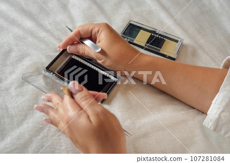 Close up master with tweezers opening pallete of fake eyelashes lying on couch, preparing for lash extension procedure. 107281084