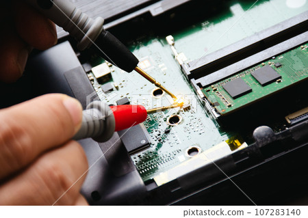 Electrician checks electronic circuit board by probe of digital multimeter. Appliance repair concept 107283140