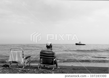 Man sitting on chair is watching an old ship sailing on sea Man sitting on chair is watching an old ship sailing on sea 107283300