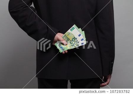 Businessman hiding euro money behind his back. Business person with euro cash money banknote Businessman hiding euro money behind his back. Business person with euro cash money banknote 107283782