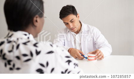 Hispanic dentist explaining to patient about teeth and how to brush with dental teeth model. The clinic treatment and healthcare concept with copy space background. Hispanic dentist explaining to patient about teeth and how to brush with dental teeth model. The clinic treatment and healthcare concept with copy space background. 107285857