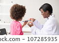 African American dentist explaining to mixed-race afro child how to brush teeth. The doctor and healthcare concept for children. 107285935