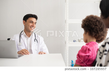 Hispanic physician meeting and diagnosis mixed-race afro children with her African American mother at a hospital. The doctor using stethoscope and do the medical exam on the laptop. 107285937