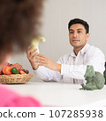 Hispanic nutritionist doctor consulting mixed-race child with her African American mother about a nutrition. Vegetables food - a new way for the good healthy and lifestyle. 107285938