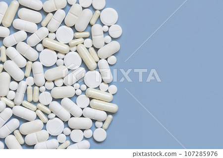 Mix of white medical capsules and pills on light blue top view, copy space. Medicinal treatment Mix of white medical capsules and pills on light blue top view, copy space. Medicinal treatment 107285976