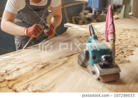 Close up of carpenter working with chisel while cutting wooden plank in carpentry workshop Close up of carpenter working with chisel while cutting wooden plank in carpentry workshop 107286033