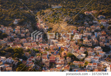 Symi Island, Greece. Greece islands holidays from Rhodos in Aegean Sea. Colorful neoclassical beautiful houses on hillsides of a Greek island during sunset. Holiday travel background. Symi Island, Greece. Greece islands holidays from Rhodos in Aegean Sea. Colorful neoclassical beautiful houses on hillsides of a Greek island during sunset. Holiday travel background. 107287844
