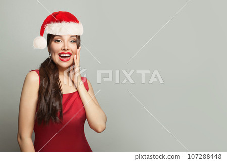 Surprised Christmas woman brunette model in Santa hat on gray background 107288448