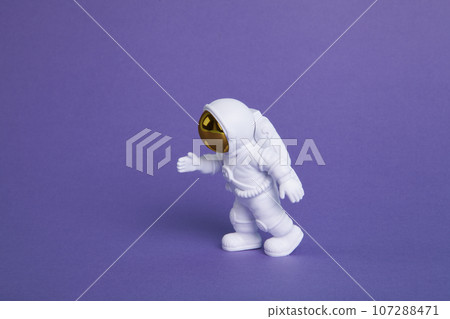 an astronaut figurine in a spacesuit exploring a plain purple background 107288471