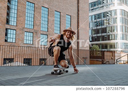 Young attractive skater performing with longboard at sunset in urban city street and smiling 107288796